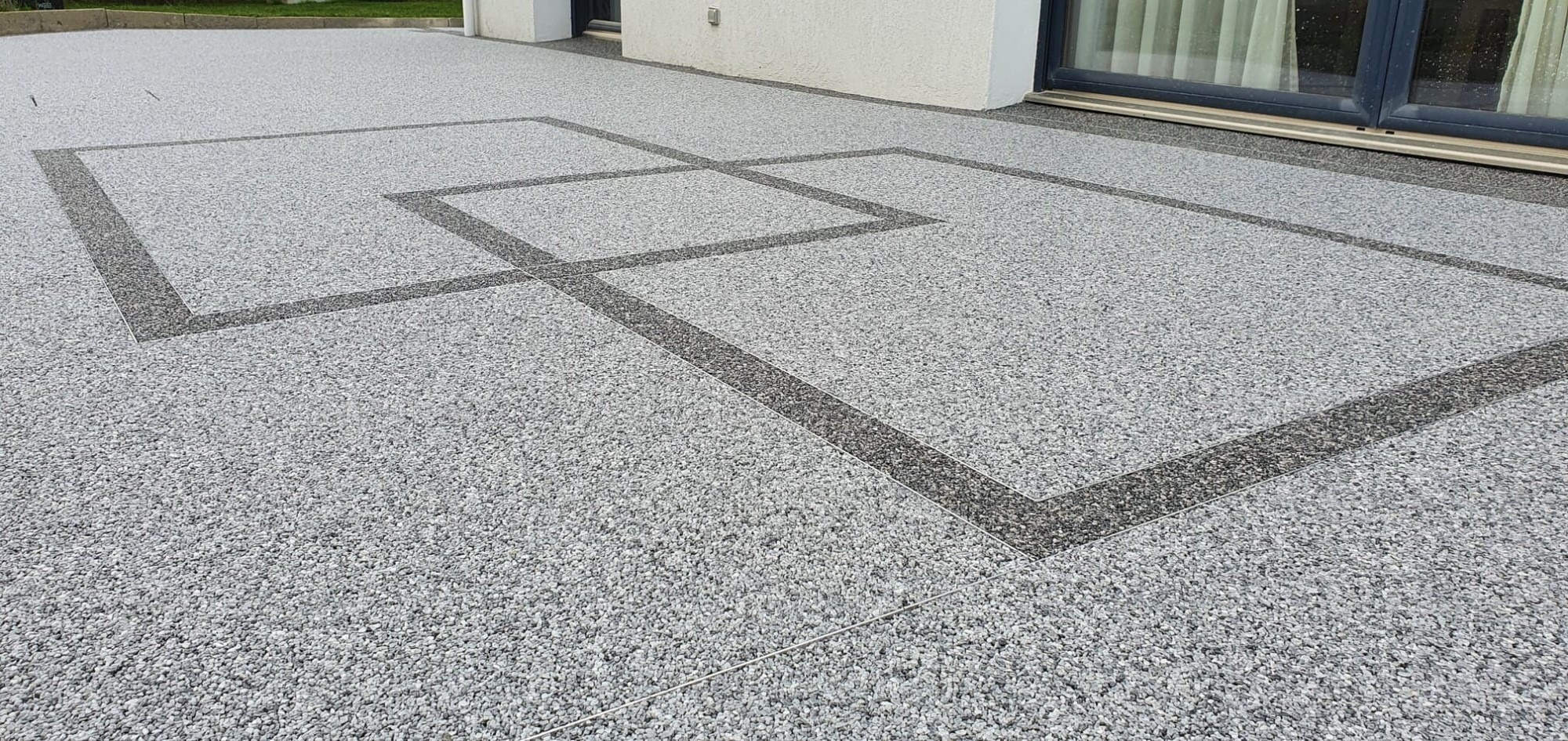 Terrasse en résine drainante grise avec motifs géométriques près d'une baie vitrée