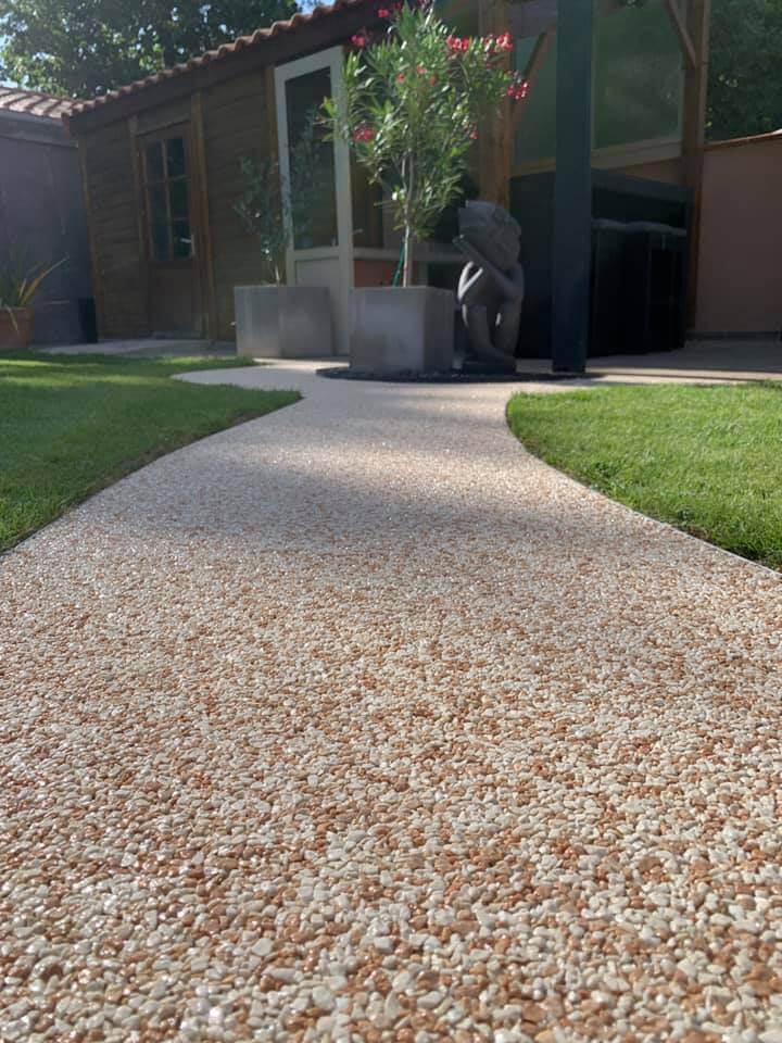 Allée de jardin en résine drainante beige menant à une maison
