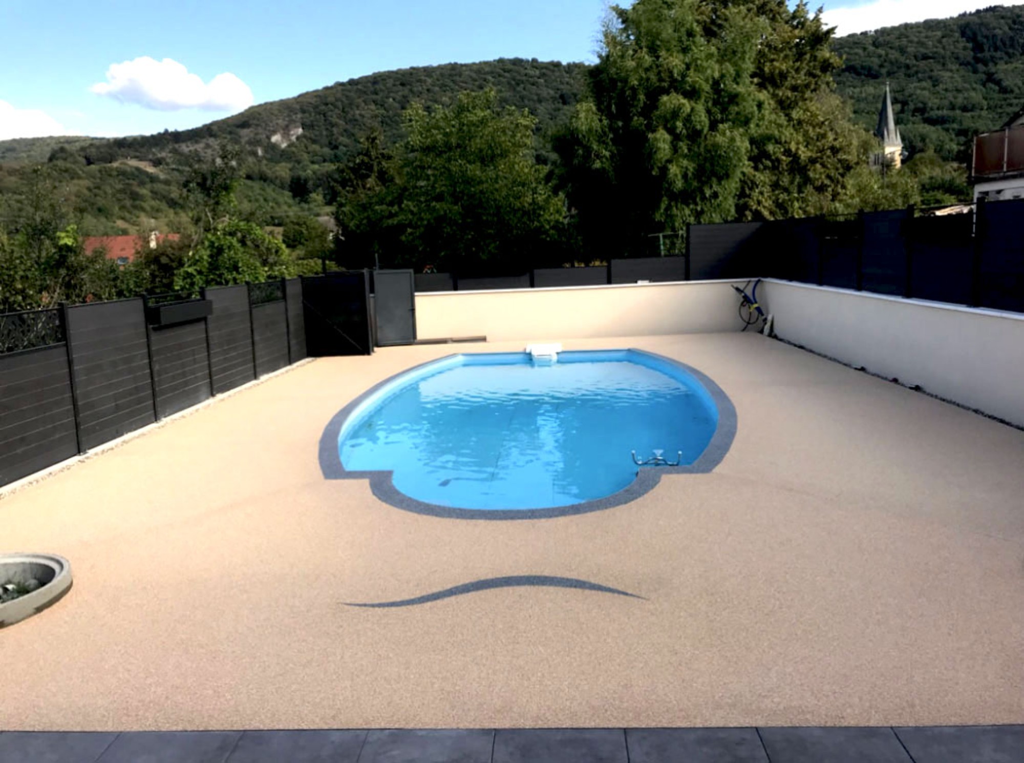 Terrasse en résine drainante beige entourant une piscine avec vue sur les collines