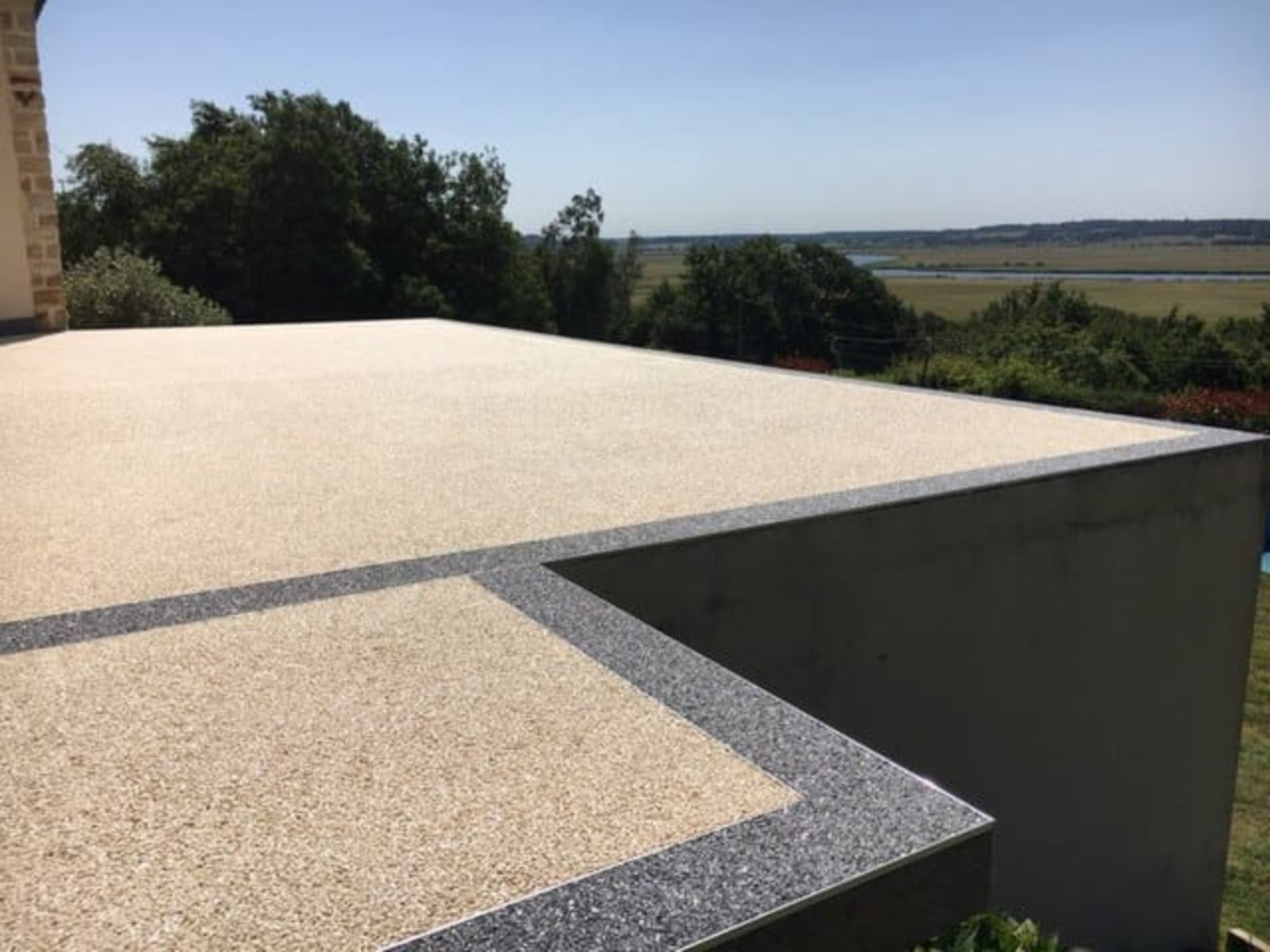 Terrasse en résine drainante avec bordure en granulat gris et vue sur la campagne