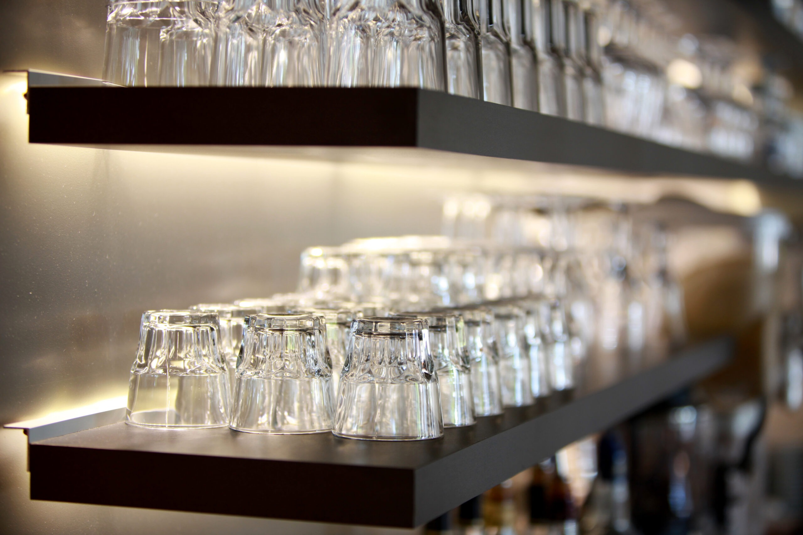 Détail des étagères éclairées et de la verrerie d'un bar aménagé par Tual Agencement